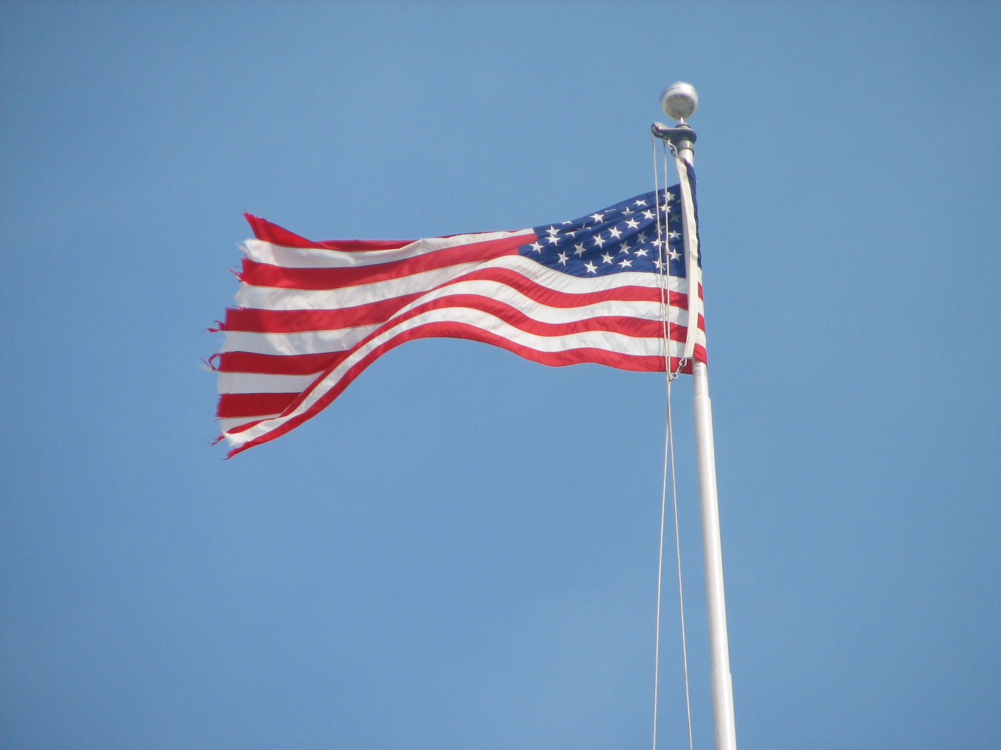 An American flag flying on a tall pole against a blue sky