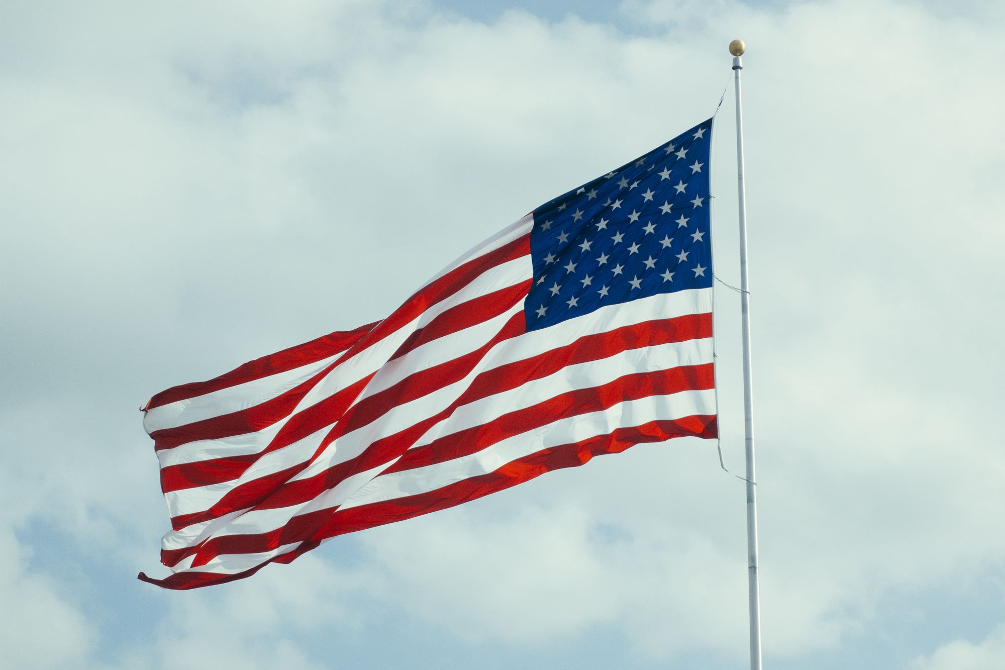 A large American flag flying against the clouds